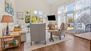 A spacious living room with a sofa, patterned armchair, wooden coffee table, and a television.