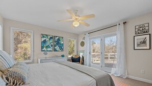 A bedroom with a bed, a ceiling fan, a window with blinds, a wall with artwork, and a motivational quote.
