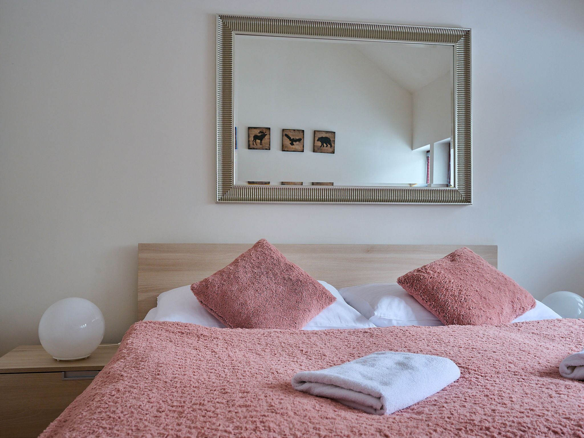 Un lit bien fait, avec une literie rose, un grand miroir au-dessus et une table de chevet avec une lampe.