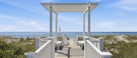 A wooden boardwalk leading to a white gazebo with a view of the beach and ocean.