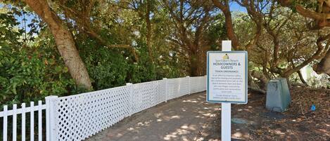 A signboard with text, a white fence, and trees.