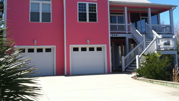 A two-story house with a pink exterior, white trim, and a covered porch with a staircase.