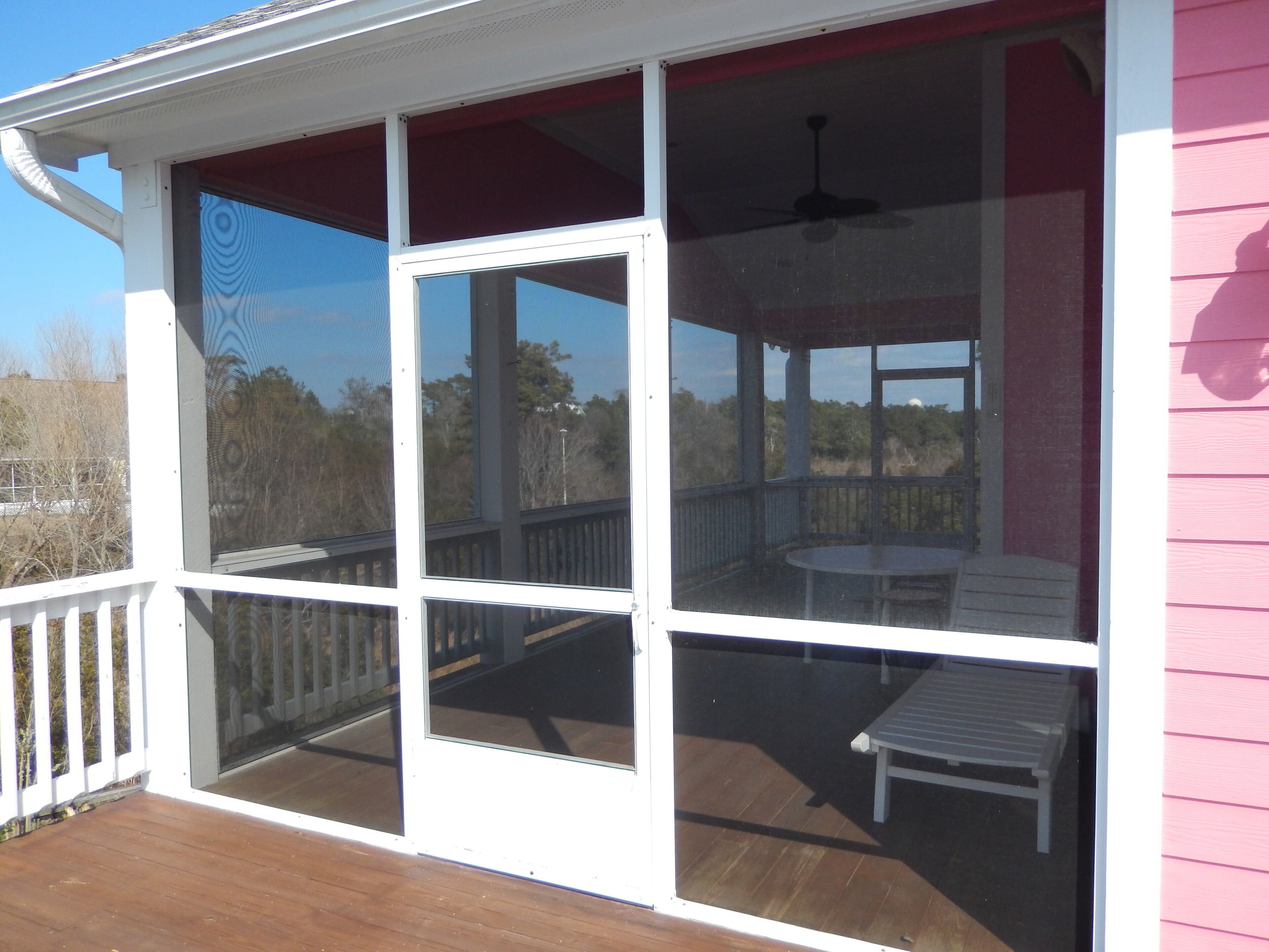 A covered outdoor deck with a table and chairs, a ceiling fan, and a view of the surrounding landscape.