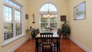 A dining area with a large table and chairs, a chandelier, and a view through a window.