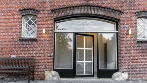 Tiilestä rakennettu rakennus, jossa on suuri kaareva sisäänkäynti, ulkona penkki ja oven yläpuolella kyltti.