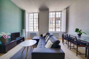 A modern living room with a sofa, a coffee table, a TV, and a dining area with chairs and a table.