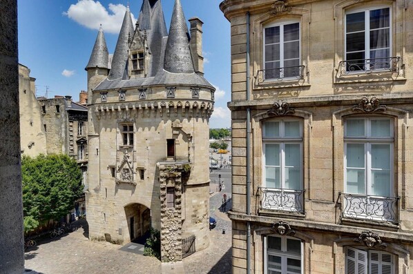 A historic stone building with a tower featuring conical roofs, a stone archway entrance, and a balcony with wrought iron railings.