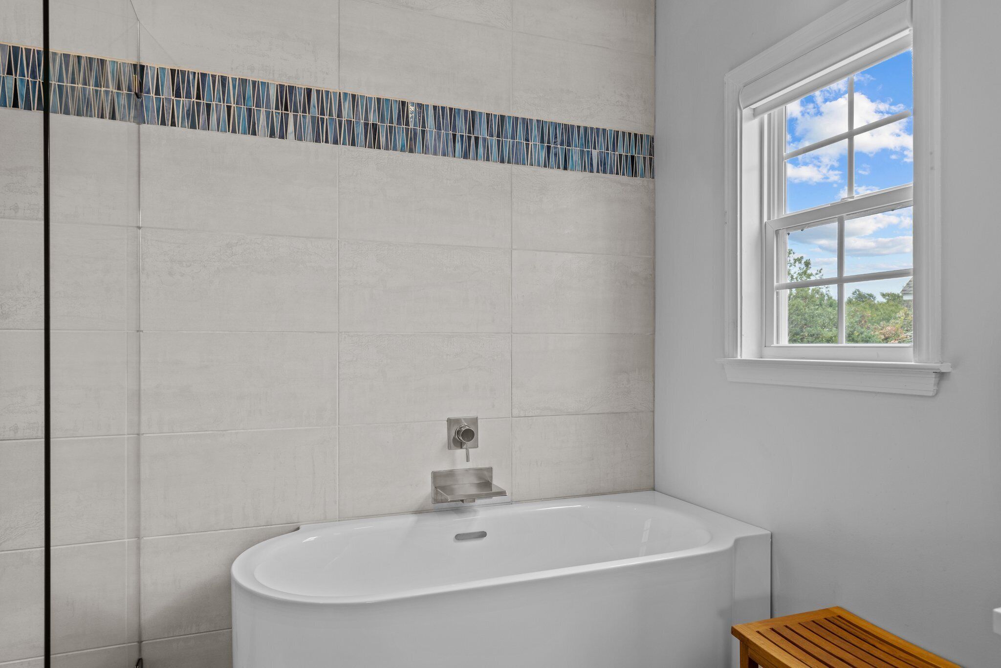 Une salle de bain avec une baignoire sur pieds, une fenêtre donnant sur un espace verdoyant et un mur recouvert de carreaux.