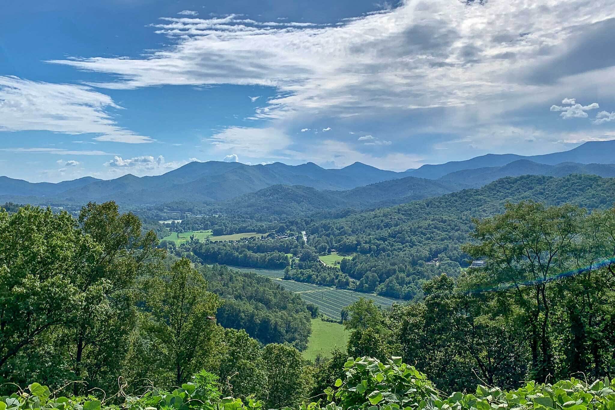 Una vista panorámica de un paisaje montañoso con un valle, bosques densos y un cielo despejado.