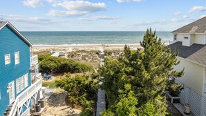 Ein Küsteneigentum mit Blick auf den Strand, einer Holzterrasse und einem blauen Gebäude.