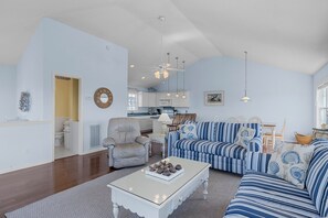 A living room with a sofa, armchair, and coffee table. There is a kitchen in the background. - 3rd Row Oceanview Duplex,beach and community pool access, in Spinnaker's Reach (Emerald Isle)