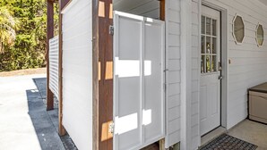 A white building with a wooden porch, a door, and a small window.