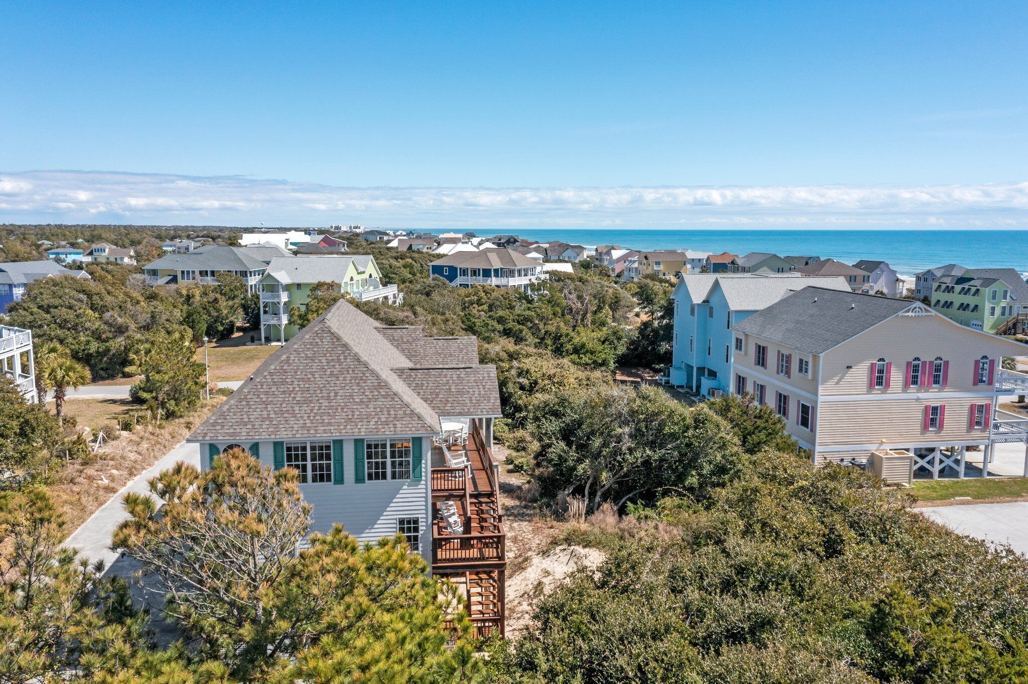 A coastal residential area with houses featuring a mix of architectural styles, including a prominent house with a wooden deck and a large bay window.