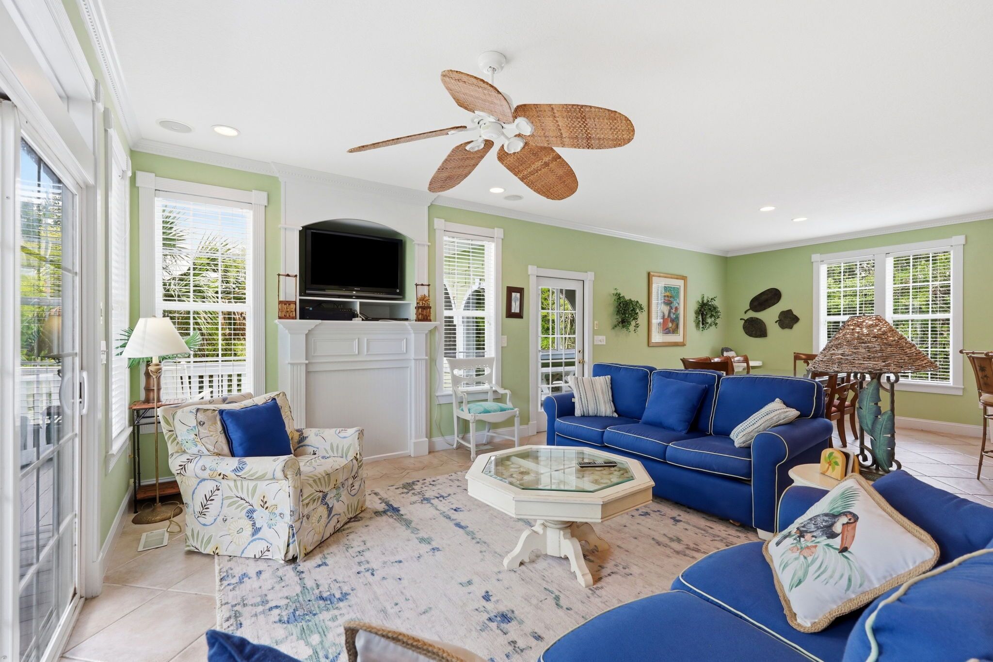 A spacious living room with a blue sofa, a glass coffee table, and a ceiling fan.