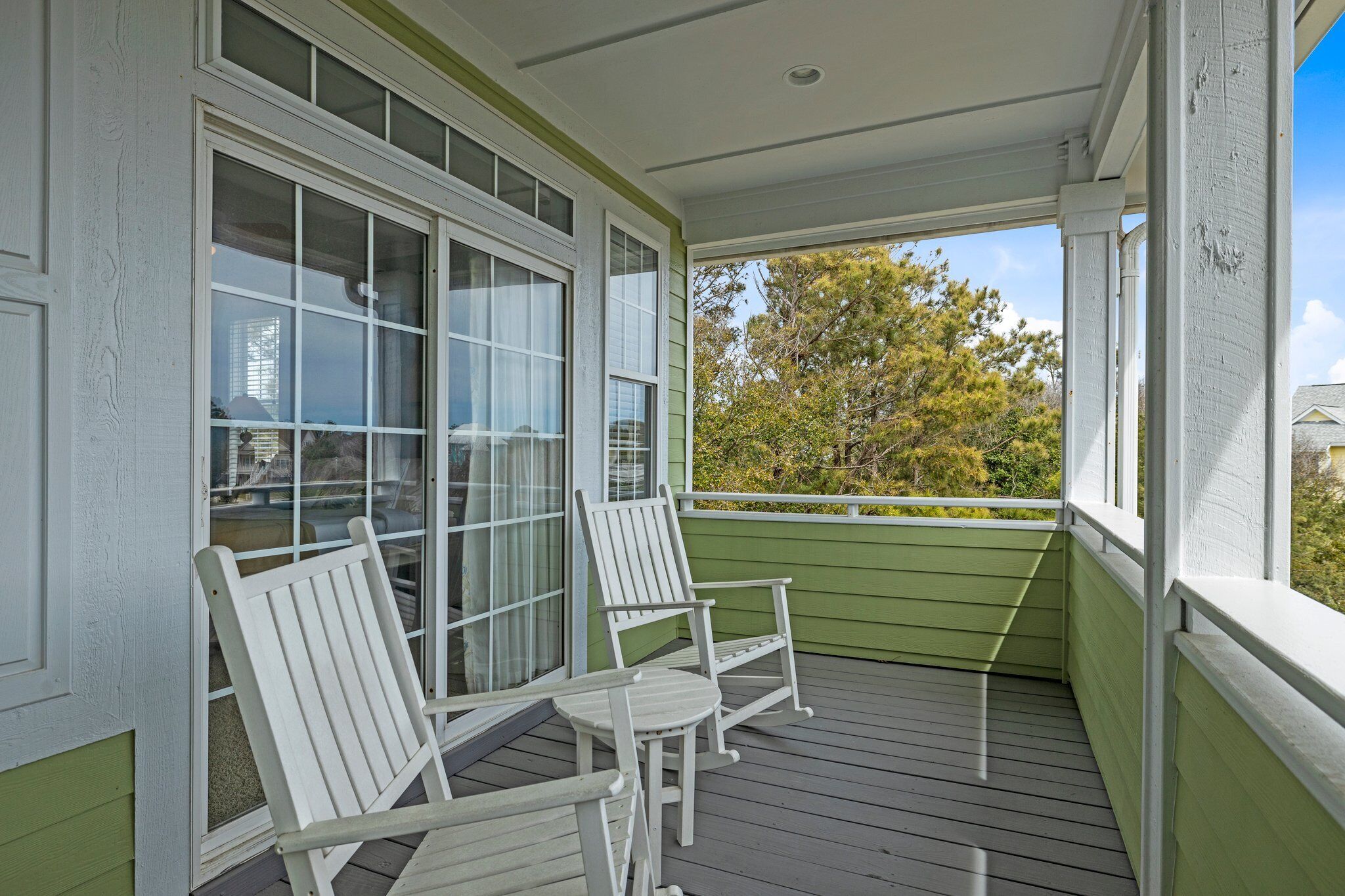 A covered porch with two white Adirondack chairs and a view of trees and buildings in the background.
