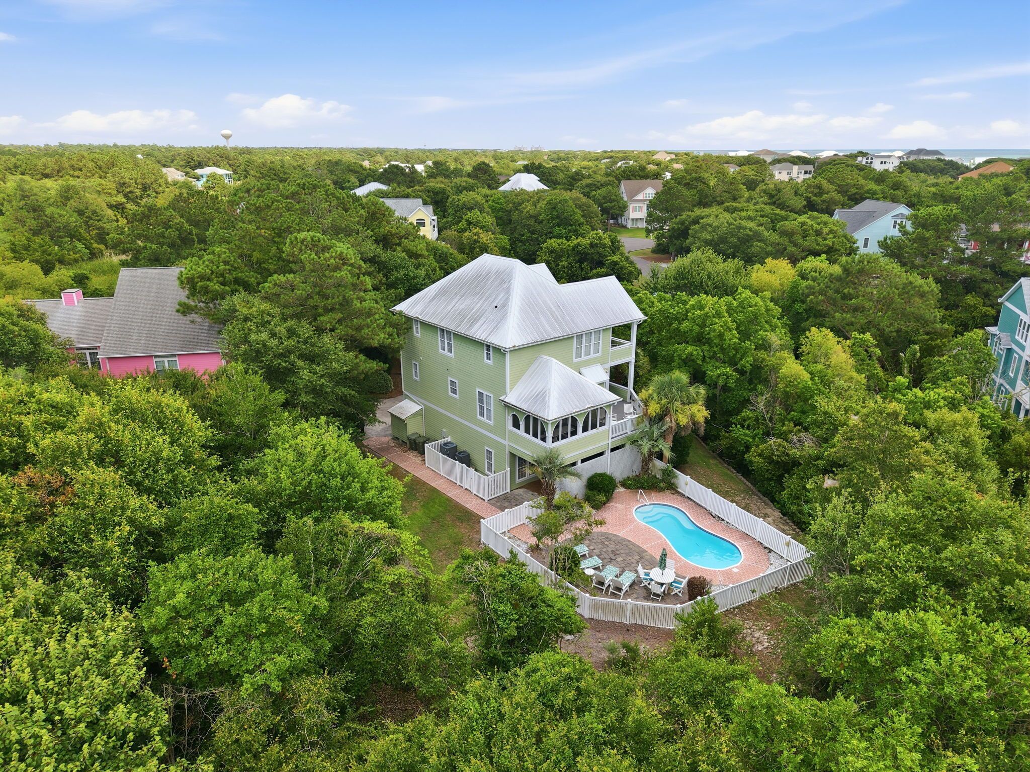 A two-story house with a pool, surrounded by dense greenery.