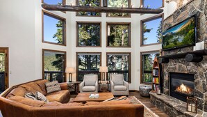 A spacious living room with a stone fireplace, large windows, and a cozy seating area. - Spacious Whitefish Mountain residence with some of the best ski in/out on the mountain. (Whitefish)