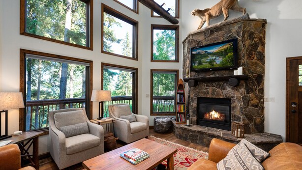A cozy living room with a stone fireplace, large windows, and a cat statue. - Spacious Whitefish Mountain residence with some of the best ski in/out on the mountain. (Whitefish)