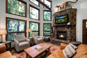 Un salón acogedor con chimenea de piedra, ventanas amplias y una estatua de un gato.