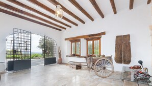 A spacious room with a high ceiling, exposed wooden beams, a large window with a view of greenery, a rustic wooden cart, and a glass table with a motorcycle model. - SON DURI (CIMENTERES) - Villa with private pool in Inca. Free WiFi (Selva)