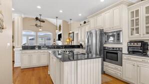 Una cocina amplia con muebles blancos, una isla central, electrodomésticos de acero inoxidable y un ventilador de techo.