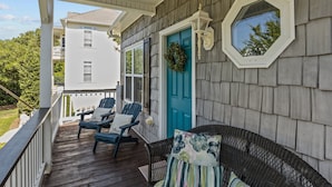 A covered porch with two Adirondack chairs, a wicker sofa, and a blue door with a wreath. - Pet Friendly, Oceanside Interior Home Private Pool, Golf Cart, and Easy Access. (Emerald Isle)