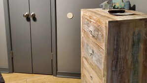 Et værelse med en grå garderobe, en trækommode, et tv ophængt på væggen og et mønstret gulv.