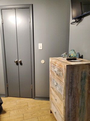 Una habitación con un armario gris, un aparador de madera, un televisor montado en la pared y un suelo estampado.