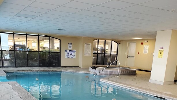 En indendørs swimmingpool med flisegulv, gelændinger og advarselsskilte.