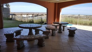 En udendørs patio med et mosaikbord og bænke, havudsigt og et træhegn i baggrunden.