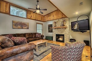 A cozy living room with a wooden ceiling, a fireplace, a television, and a large window. - Two Trees - A Unique Custom Cabin (Rockbridge)
