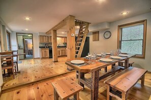 Un comedor amplio con una mesa de madera dispuesta para seis personas, una escalera de madera y vista a la cocina al fondo.