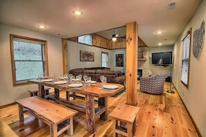 A dining area with a wooden table set for six, benches, and a sofa in the background.