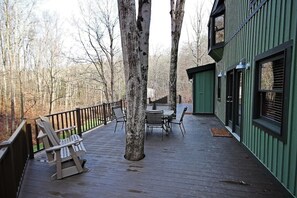 Una terraza de madera con mobiliario exterior, rodeada de árboles.