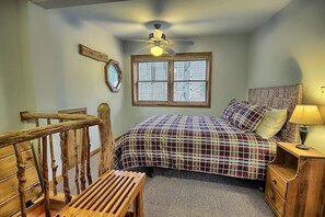 A bedroom with a bed, a wooden chair, a nightstand with a lamp, a ceiling fan, and a window with blinds.