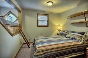 A bedroom with a bed, a window, a ladder, and a shelf.