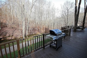Une terrasse dotée d’un barbecue, entourée d’une rambarde en bois, et offrant une vue sur une zone boisée.