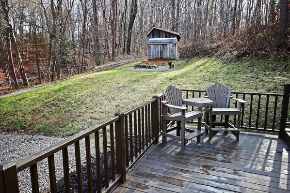 A wooden deck with a table and chairs, a small shed, and a grassy area with trees in the background.