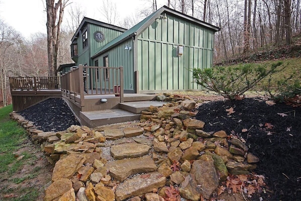 Un chalet rustique avec un sentier de pierres menant à l’entrée, entouré d’une zone boisée.