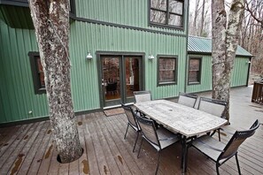 A green building with a wooden deck, a table with chairs, and a door leading inside.