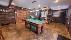 A pool table in a room with wooden walls and a ceiling fan.