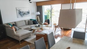 Una sala de estar moderna con un sofá, una mesa de centro y sillas, un ventanal con vistas, y un cuadro en la pared.