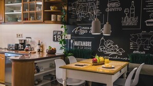 Una cocina con pared de pizarra, armarios de madera y una zona de comedor con mesa para dos.