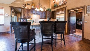 A kitchen with dark wooden cabinets, a central island with chairs, and a hanging light fixture. - Waterfront Homes on Lake Travis (Spicewood)
