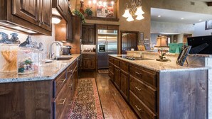 A spacious kitchen with wooden cabinets, a large island, stainless steel appliances, and a decorative rug. - Waterfront Homes on Lake Travis (Spicewood)