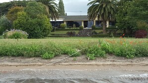 A beachfront property with a well-maintained garden, palm trees, and a house with a large window overlooking the sea. - Lake front luxury at your door step (Ngongotaha)
