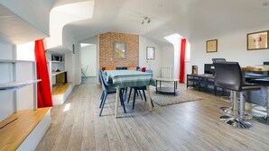 A modern living room with a dining area, a brick accent wall, and a kitchen in the background. - The Heart of Amboise, three-room apartment, two bedrooms in the city center (Amboise)