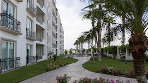 A pathway leading to a multi-story building with balconies, surrounded by well-maintained grass and flowering plants.
