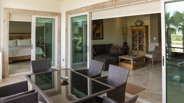 A modern living area with a glass table, wicker chairs, a sofa, and a cabinet.