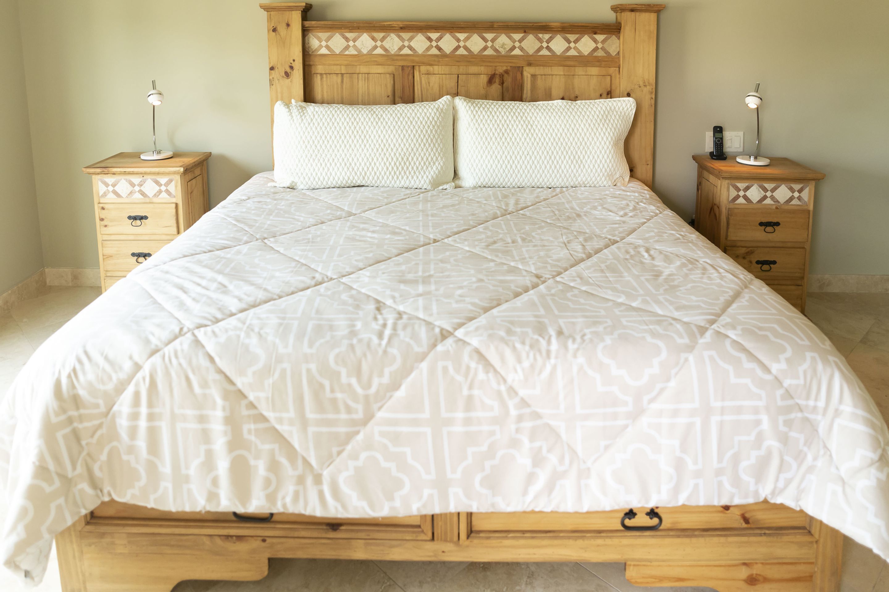 A bed with a quilted white cover, two bedside tables with lamps, and a wooden headboard.